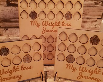 May include: Three wooden coin holders with the text "My Weight Loss Journey" on each. The holders are made of light brown wood and have a slot for each coin. The holders are standing on a wooden surface.