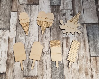 May include: Wooden cutouts of ice cream cones and popsicles. The ice cream cones have a waffle cone texture and the popsicles have different textures, including a striped texture and a textured surface. The cutouts are on a wood background.