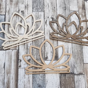 Puede incluir: Tres recortes de madera de flores de loto en diferentes tonos de marrón. Los recortes están dispuestos en una fila sobre un fondo de veta de madera.