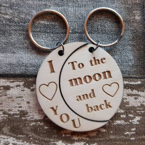 May include: A wooden keychain with two connected circles. One circle says "I love you" with a heart. The other circle says "To the moon and back" with a heart.