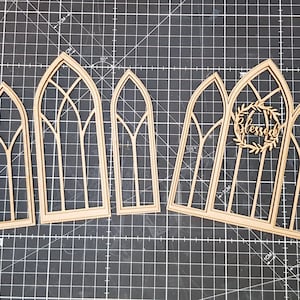 Puede incluir: Cinco recortes de marco de ventana de madera con un diseño de arco gótico. El recorte central tiene una corona con la palabra "Blessed" dentro.