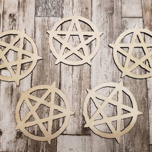 Pode incluir: Cinco formas de pentagrama de madeira, cada uma com um desenho de estrela de cinco pontas, estão dispostas sobre uma superfície de madeira castanho claro.
