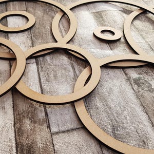 Könnte beinhalten: Ein Satz aus sieben Holzringen in verschiedenen Größen, die in einem Kreis auf einem Holzgrund angeordnet sind. Die Ringe sind alle aus dem gleichen Material gefertigt und haben eine natürliche Holzoptik.