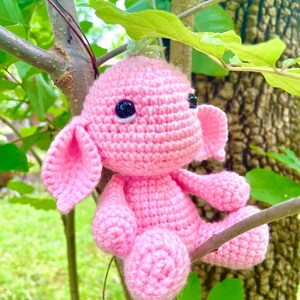 K&ouml;nnte beinhalten: Ein rosa geh&auml;keltes Stofftier mit gro&szlig;en Ohren und schwarzen Augen. Das Tier sitzt auf einem Ast.