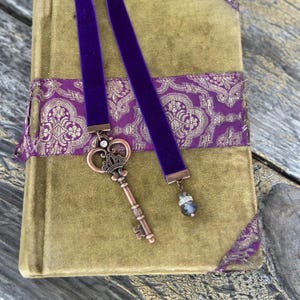 Marcapáginas de edición limitada con cinta de terciopelo morado: Llave grande de cobre con dije de corona y cristal.