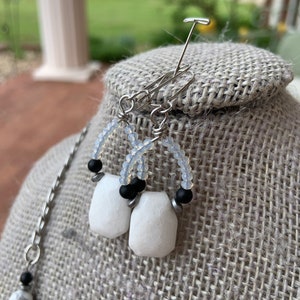 May include: A pair of earrings with white and black beads and white stone accents. The earrings are hanging from a silver wire.