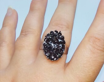 May include: A silver ring with a large oval-shaped black gemstone. The gemstone is set in a prong setting and has a textured surface.