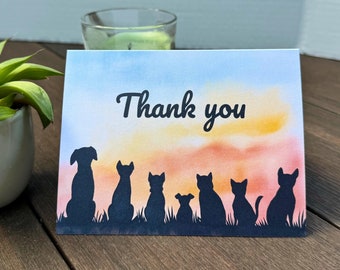 May include: Thank you card with a watercolor sunset background and silhouettes of a dog and cats. The card says "Thank you" in black cursive.