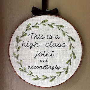 May include: Embroidered hoop art with a white background and green leaves surrounding the text "This is a high-class joint act accordingly".