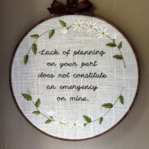 May include: Embroidered hoop with white daisies and green leaves around the text "Lack of planning on your part does not constitute an emergency on mine."