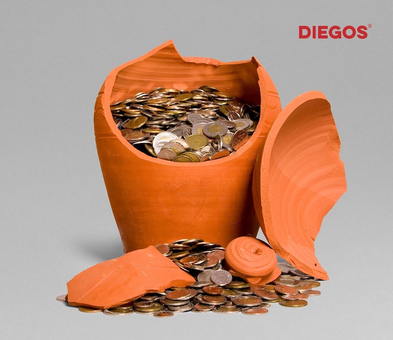 May include: A broken terracotta piggy bank overflowing with coins. The orange ceramic pot is shattered, with coins spilling out onto the surface. The logo "DIEGOS" is visible in the upper right corner.