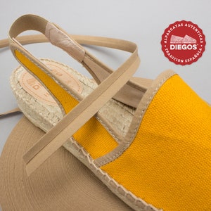 May include: Yellow canvas espadrille sandals with a tan strap and jute sole. The sandals have a tan elastic strap that goes around the ankle. The brand name "DIEGOS" is visible on the sole.