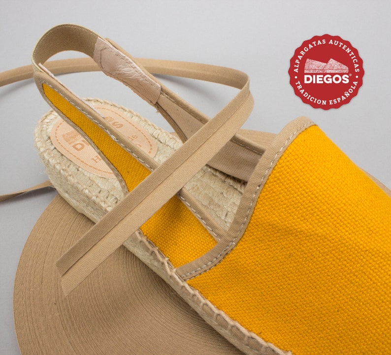 May include: Yellow canvas espadrille sandals with a tan strap and jute sole. The sandals have a tan elastic strap that goes around the ankle. The brand name "DIEGOS" is visible on the sole.