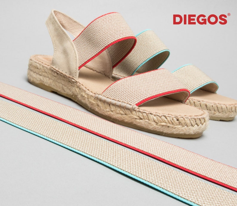 May include: Beige espadrille sandals with red and blue elastic straps. The sandals have a jute wedge sole and are made by the brand "DIEGOS".