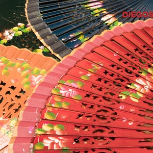 May include: Three hand fans with painted floral designs. The top fan is black with gold trim, the middle fan is orange with gold trim, and the bottom fan is red with gold trim. The fans are folded and have a decorative cut-out design.