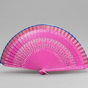 May include: A bright pink hand fan with a decorative pattern. The fan has a blue trim along the top edge and a silver metal ring at the base. The fan's surface is decorated with a repeating pattern in a lighter shade of pink.