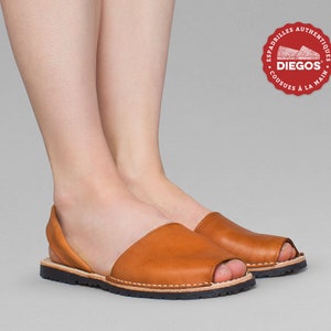 Puede incluir: Un par de alpargatas de cuero marr&oacute;n con puntera abierta y suela de goma negra. Los zapatos son hechos a mano y tienen un detalle cosido alrededor de la punta y el tal&oacute;n.
