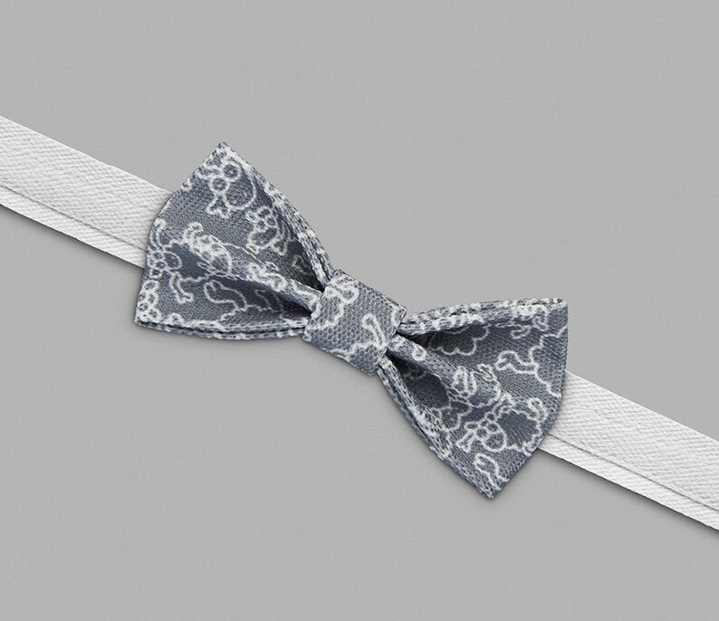 May include: A gray bow tie with a white floral pattern. The bow tie is tied and ready to wear.