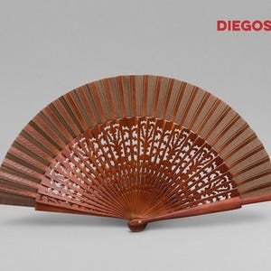 May include: A brown wooden hand fan with a carved design. The fan is closed and has a brown and beige striped pattern on the back.