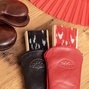 May include: A collection of Spanish flamenco accessories, including a pair of brown castanets, two decorative fans, and two leather fan cases. One fan is red with white polka dots, and the other is black with white shapes. The cases are black and red.