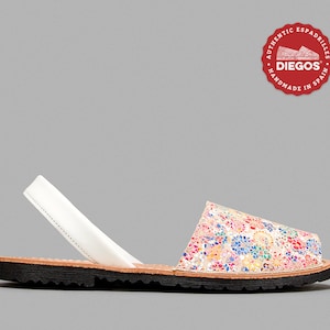 Może przedstawiać: Pojedynczy sandał espadryle z kwiatowym wzorem w kolorze r&oacute;żowym, niebieskim, ż&oacute;łtym i białym. Sandał ma biały pasek, brązową wkładkę i czarną podeszwę. Logo marki jest widoczne w prawym g&oacute;rnym rogu.