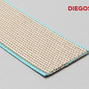 May include: A close-up of a beige woven fabric with a light blue trim. The fabric is textured and has a subtle sheen. The fabric is labeled "DIEGOS".