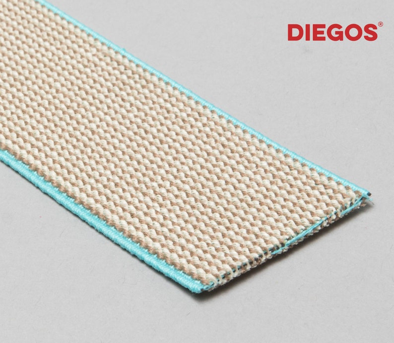 May include: A close-up of a beige woven fabric with a light blue trim. The fabric is textured and has a subtle sheen. The fabric is labeled "DIEGOS".