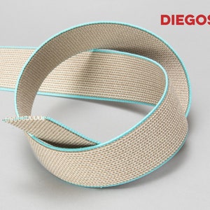 May include: Beige elastic webbing with a turquoise trim. The webbing is woven with a textured pattern.