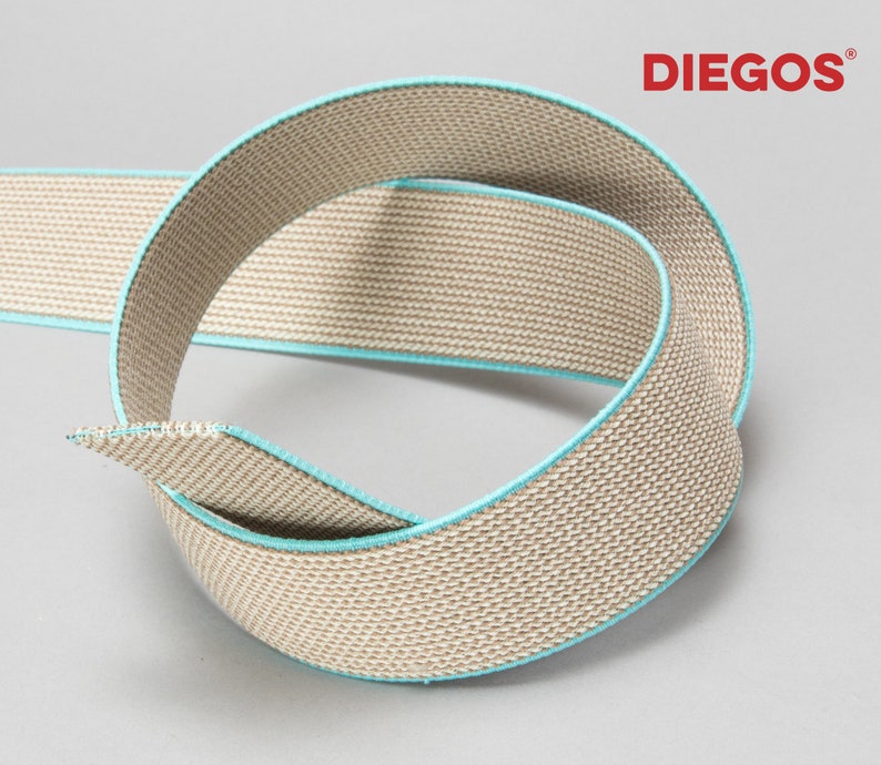 May include: Beige elastic webbing with a turquoise trim. The webbing is woven with a textured pattern.