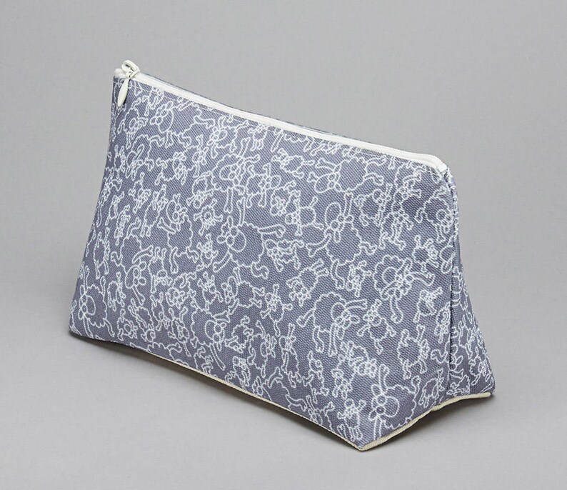 May include: A gray zippered pouch with a white pattern of small animals. The pouch is made of a soft, fabric material.