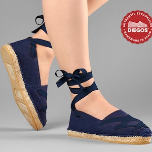 May include: Navy blue espadrille shoes with a lace-up design. The shoes have a jute sole and are handmade in Spain. The label reads "Authentic Espadrilles Diegos Handmade in Spain".