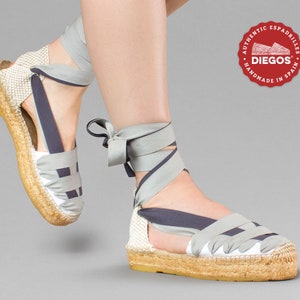 Pode incluir: Sapatos de esparto cinzentos e azul marinho com design tecido e atacadores amarrados. Os sapatos são da marca "DIEGOS" e são feitos à mão em Espanha.