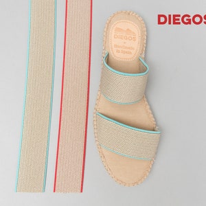 May include: Two beige fabric straps with a blue and red trim. A pair of beige espadrille sandals with a blue trim and a leather label that reads "DIEGOS Handmade in Spain".