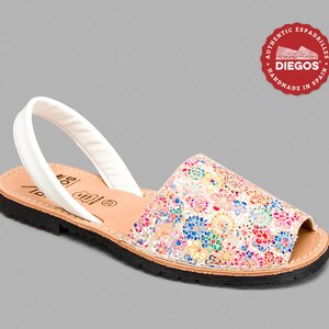 Może przedstawiać: Sandał w kwiatowy wz&oacute;r z białym paskiem. Sandał ma kolorowy wz&oacute;r z r&oacute;żowymi, niebieskimi, ż&oacute;łtymi i zielonymi kwiatami. Podeszwa jest czarna, a wkładka beżowa. Okrągłe logo m&oacute;wi "DIEGOS" i "AUTHENTIC ESPADRILLES HANDMADE IN SPAIN."