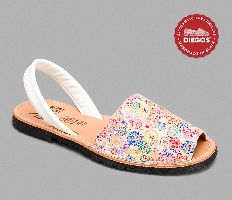 Może przedstawiać: Sandał w kwiatowy wz&oacute;r z białym paskiem. Sandał ma kolorowy wz&oacute;r z r&oacute;żowymi, niebieskimi, ż&oacute;łtymi i zielonymi kwiatami. Podeszwa jest czarna, a wkładka beżowa. Okrągłe logo m&oacute;wi "DIEGOS" i "AUTHENTIC ESPADRILLES HANDMADE IN SPAIN."
