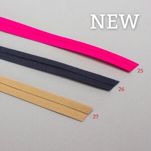 May include: Three different colors of bias tape, pink, navy blue, and beige. The tape is folded in half and has a seam down the center. The tape is labeled with numbers 25, 26, and 27.