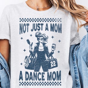 Könnte beinhalten: Ein graues T-Shirt mit einer Grafik einer Frau, die eine Haarbürste und eine Tasse Kaffee hält. Der Text auf dem Shirt lautet "Not Just a Mom A Dance Mom".