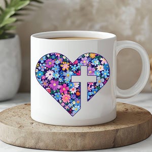 May include: White ceramic mug featuring a heart-shaped floral design in shades of blue, purple, pink, and yellow, with a white cross in the center. The mug is on a wooden coaster.