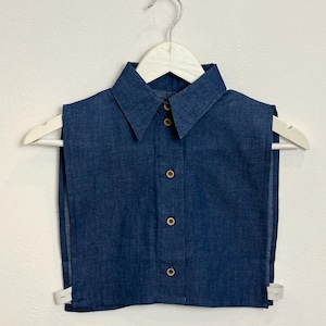 Könnte beinhalten: Ein Denim-Kragen mit Knopfverschluss. Der Kragen ist blau und hat einen weißen Kleiderbügel.