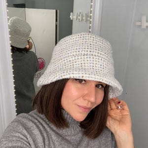 May include: A white and blue patterned bucket hat with a soft, fuzzy texture. The hat is made of a knitted fabric and has a wide brim.