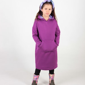 May include: A young person wearing a purple hooded sweatshirt dress with a tie-dye headband. The sweatshirt has a large front pocket and the person is wearing colorful patterned rain boots.