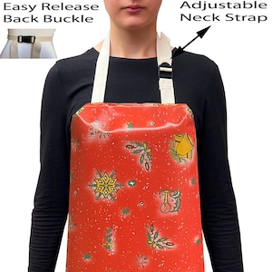 May include: Red waterproof apron with a Christmas pattern featuring snowflakes, holly, and bells. The apron has an adjustable neck strap and an easy release back buckle.