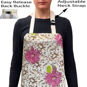 May include: An apron with a floral design. The apron features a pattern of white pebbles and pink flowers. It has an adjustable neck strap and an easy-release back buckle. The apron is made of a durable material.