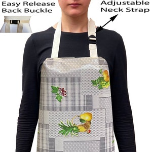 May include: A grey apron with a fruit and vegetable design. The apron has an adjustable neck strap and an easy-release back buckle. The apron features a pattern of squares and rectangles with images of pears, grapes, and other produce.