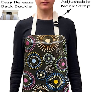 May include: A black apron with a colourful circle pattern. The apron has an adjustable neck strap and an easy release back buckle.