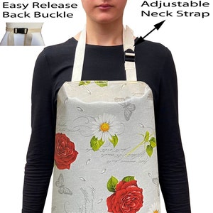 May include: A grey apron with a floral pattern featuring red roses, white daisies, and butterflies. The apron has adjustable neck straps and an easy release back buckle.