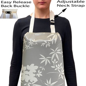 May include: A grey waterproof apron with a white floral pattern. The apron has an adjustable neck strap with a buckle and an easy release back buckle.