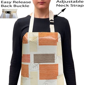 May include: A white apron with a geometric pattern of orange, brown, and beige rectangles and leaves. The apron has an adjustable neck strap and an easy release back buckle.