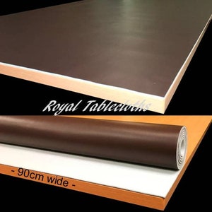 May include: A brown, rolled-up tablecloth with a white backing. The tablecloth is 90cm wide. The tablecloth is rolled up on a wooden table.