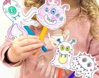 May include: Four colorful monster puppets on wooden sticks. The puppets are hand-drawn with various designs, including an octopus, a cloud-like creature, and two other unique monsters. The puppets are held by a person wearing a pink sweater.